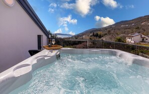 A hot tub with a wooden tray holding a bottle of wine and a glass, set against a backdrop of a mountainous landscape and a clear sky. - Gorgeous home in Lovran with sauna (Lovran)