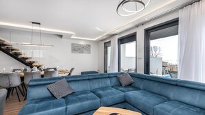 Un salon moderne avec un canapé d’angle bleu, un coin repas avec une table et des chaises en bois, et un escalier menant à un niveau supérieur.