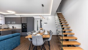 Une cuisine moderne avec des meubles gris, un four encastré et un coin repas comprenant une table en bois et des chaises grises.