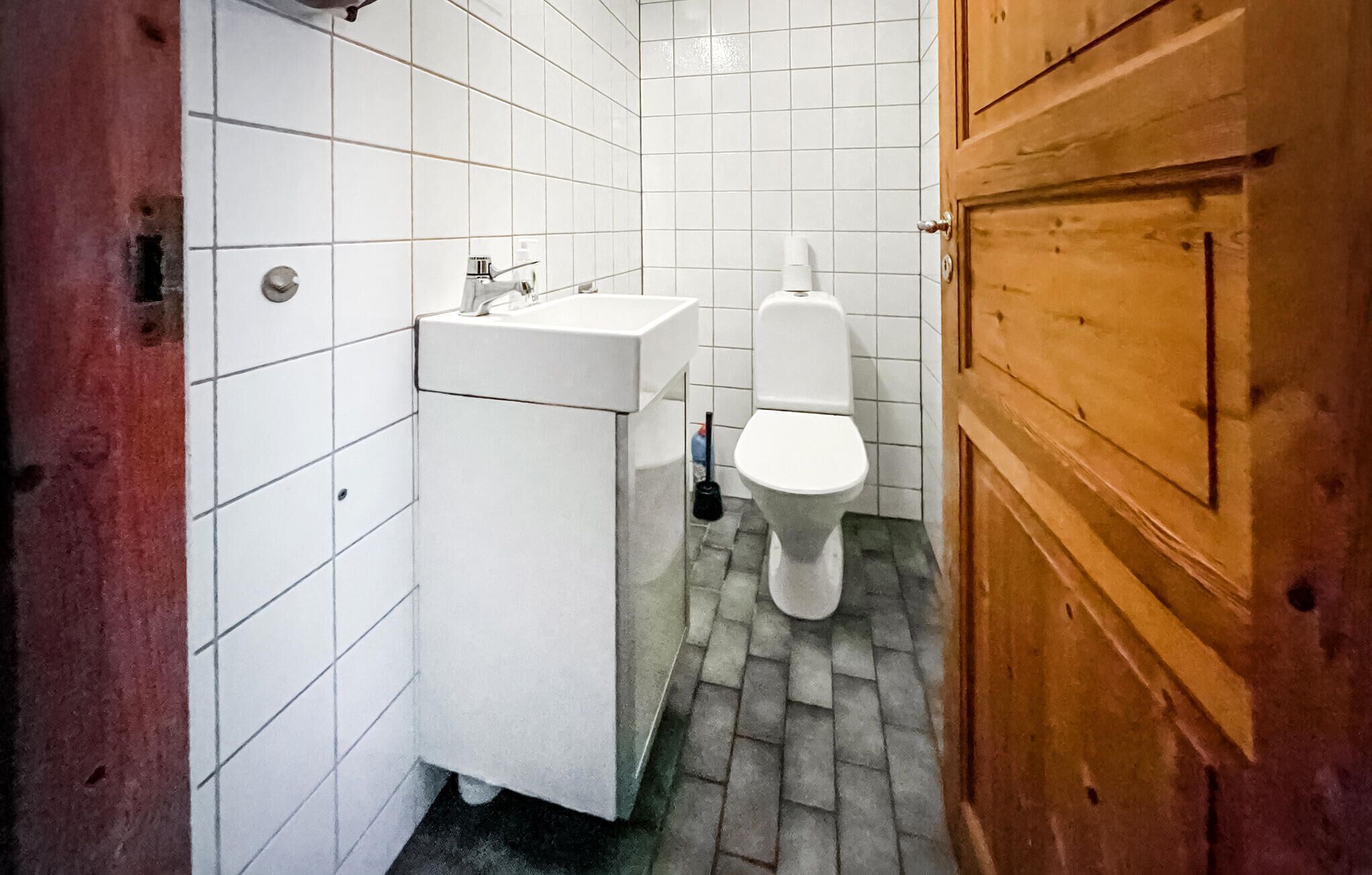 A small, compact bathroom with white tiles, a sink, and a toilet.