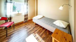 A small room with a wooden floor, a single bed with pillows, a chair, a table, and a window with curtains. - Nice apartment in Höör (Höör)