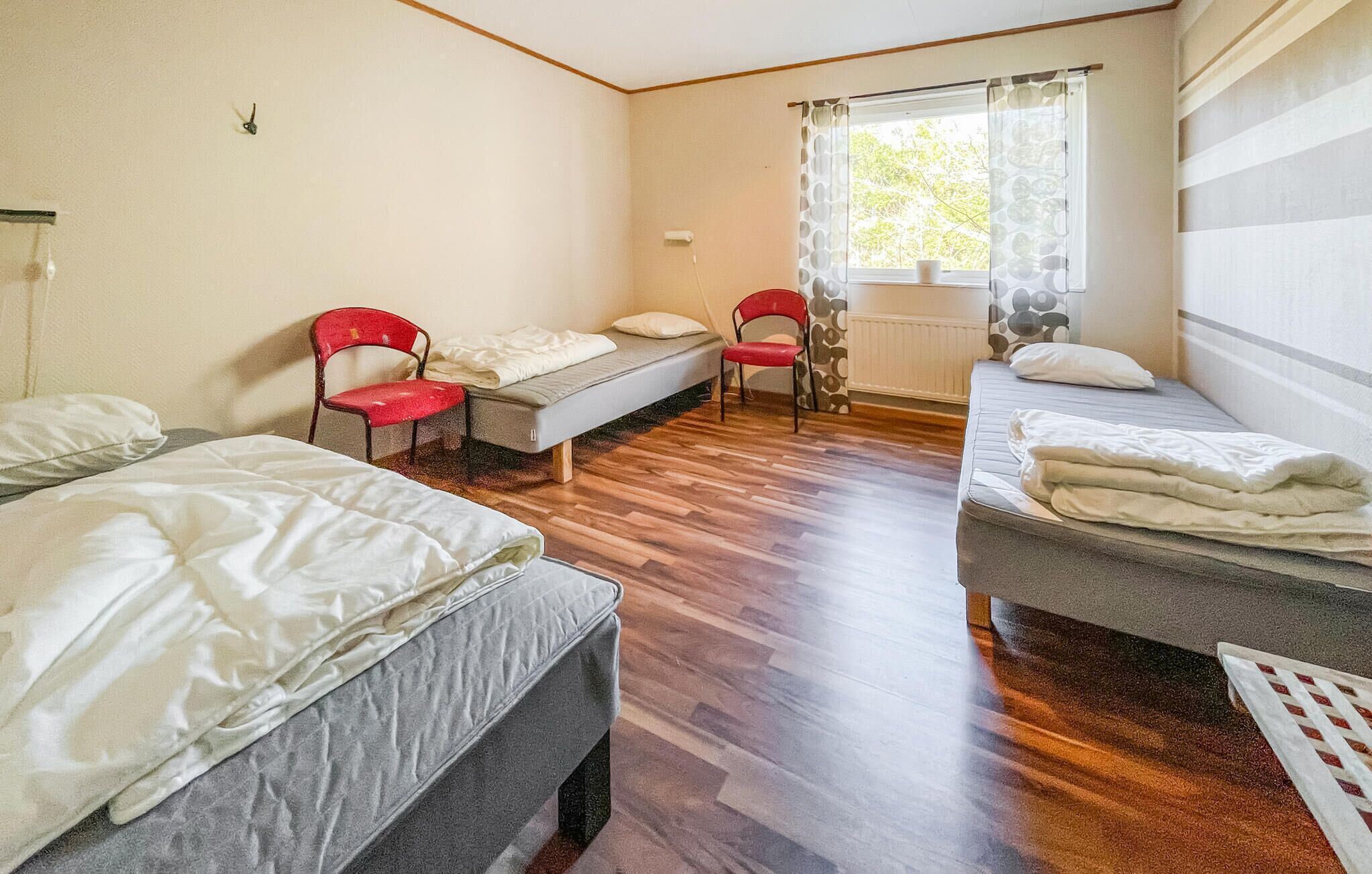 Een kleine, gezellige kamer met twee eenpersoonsbedden, een rode stoel en een raam met uitzicht op bomen.