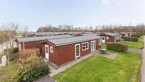 A row of red wooden mobile homes with grey roofs, arranged in a neat row with green lawns and trimmed bushes in front. - Amazing home in Wagenborgen with WiFi (Wagenborgen)