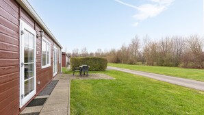 A single-story building with a red exterior, a front door, and a small patio area with a table and chairs. - Amazing home in Wagenborgen with WiFi (Wagenborgen)