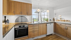 A modern kitchen with wooden cabinets, a stainless steel range hood, a dishwasher, and a large window providing natural light.