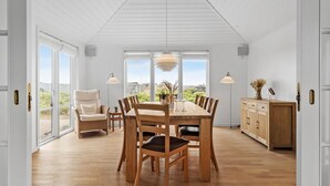 A spacious dining area with a high ceiling and large windows, wooden furniture, and a view of the outdoors.