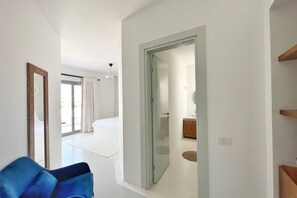 Ein modernes Hotelzimmer mit einem großen Bett, einer Glastür zu einem Badezimmer und einem blauen Sessel.