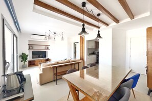Une cuisine moderne avec des poutres en bois, un coin repas avec une table en verre et un salon avec un canapé et un téléviseur.