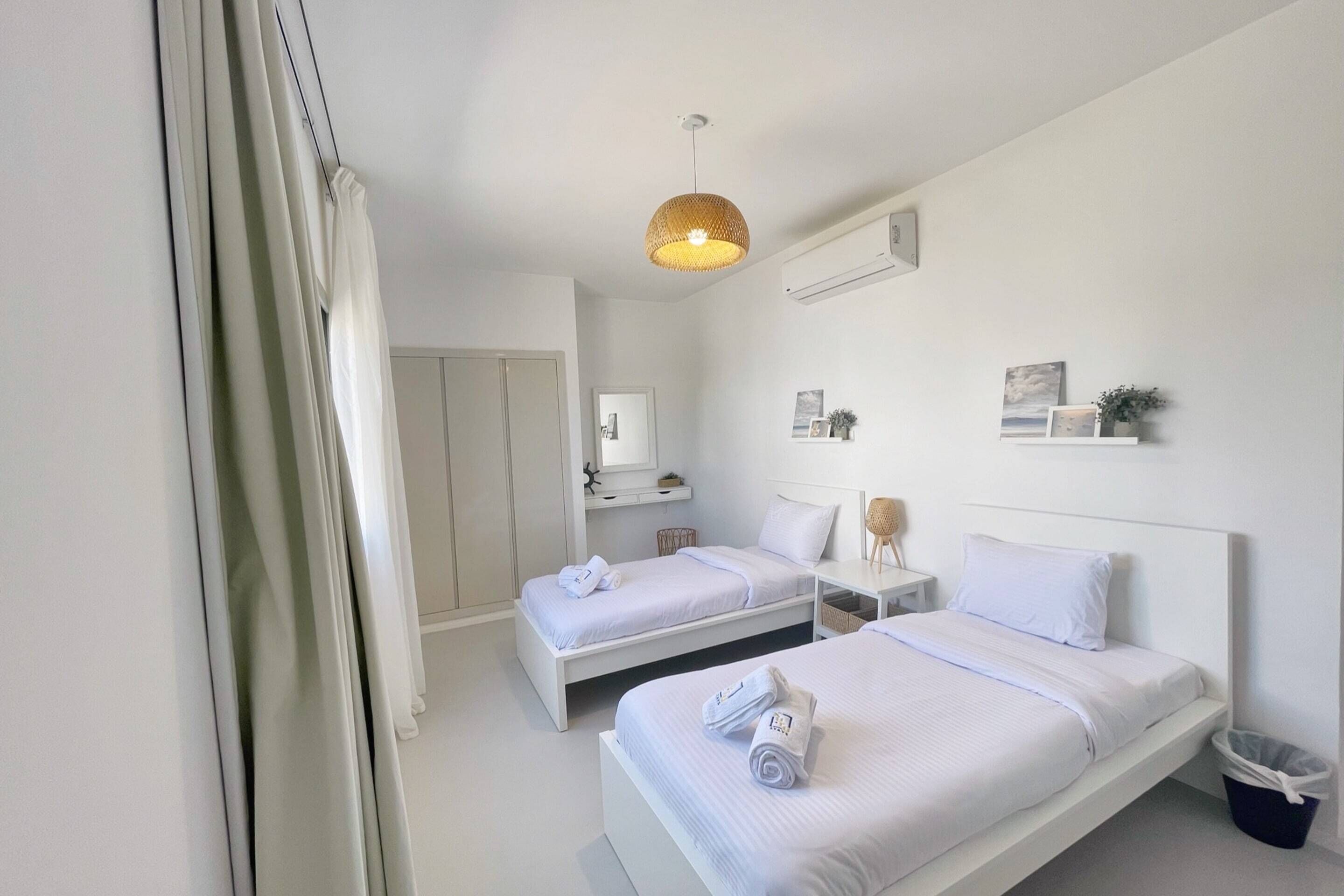 Habitación de hotel con dos camas, una lámpara colgante, una mesita de noche pequeña, aire acondicionado de pared y un cesto de basura.