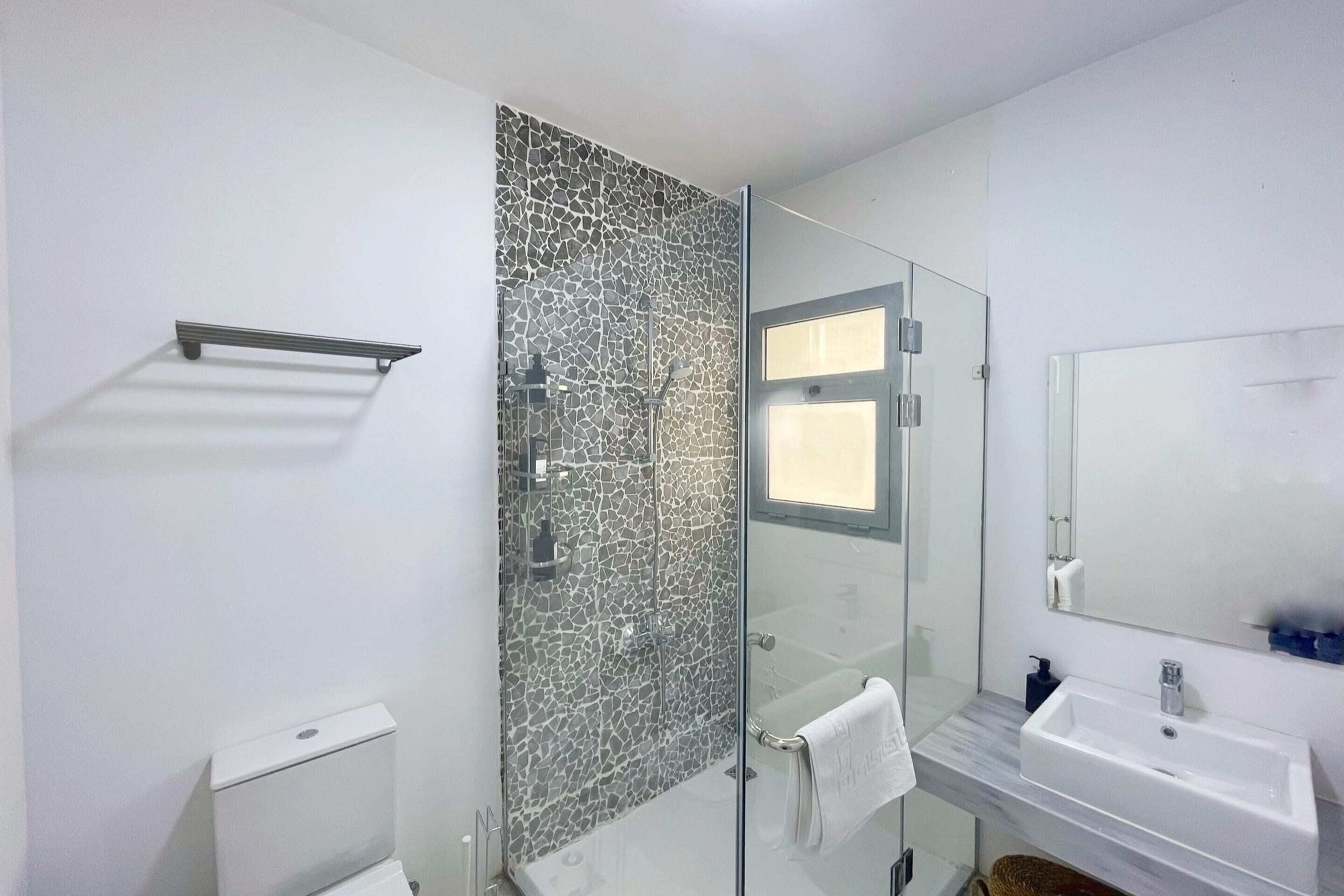 Un baño moderno con cabina de ducha de vidrio, un lavamanos blanco y un espejo grande.