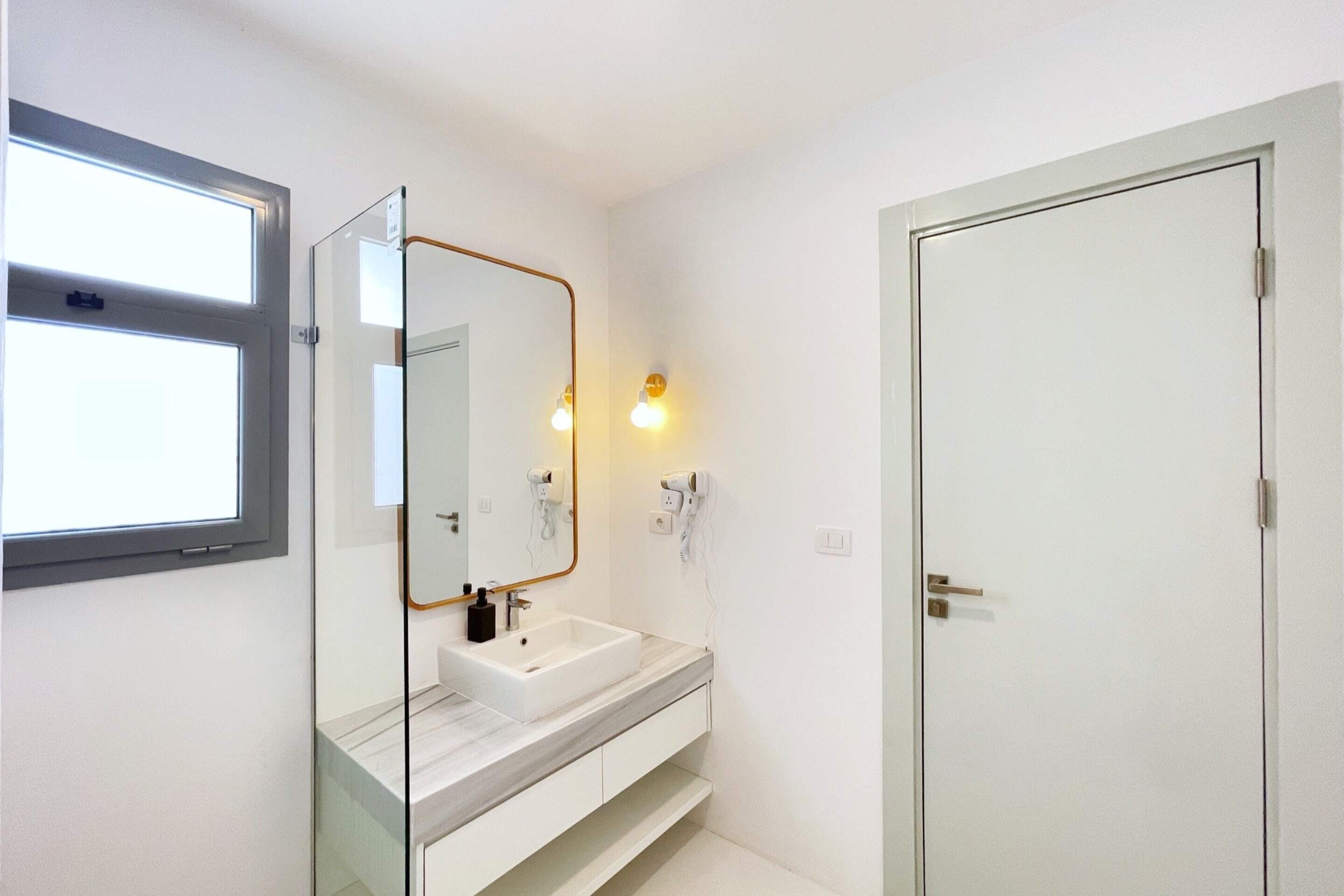 Un baño con un lavamanos blanco, un espejo con marco dorado y una puerta con picaporte.