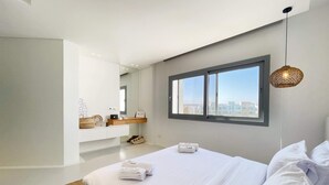 Een moderne slaapkamer met een groot bed, een raam met uitzicht op de stad, een nachtkastje en een hanglamp.