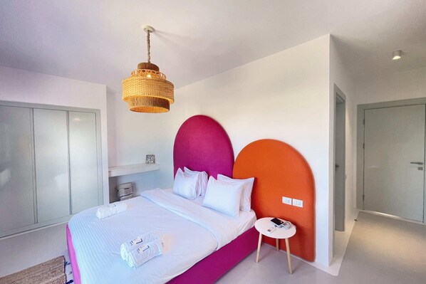 A modern bedroom with a bed, a bedside table, a hanging light fixture, and a wardrobe.