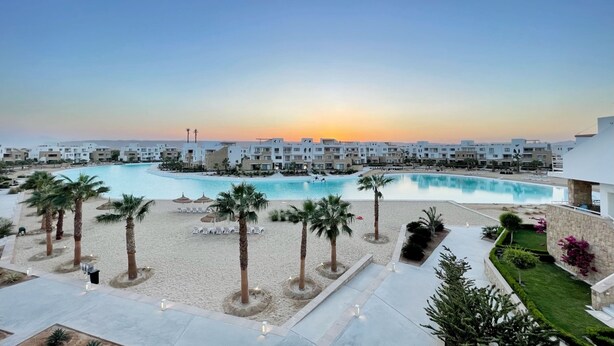 Een resort met een groot zwembad, palmbomen en een strandgebied.