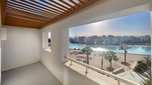 Een balkon met een houten plafond en uitzicht op een strand met palmbomen en een zwembad.