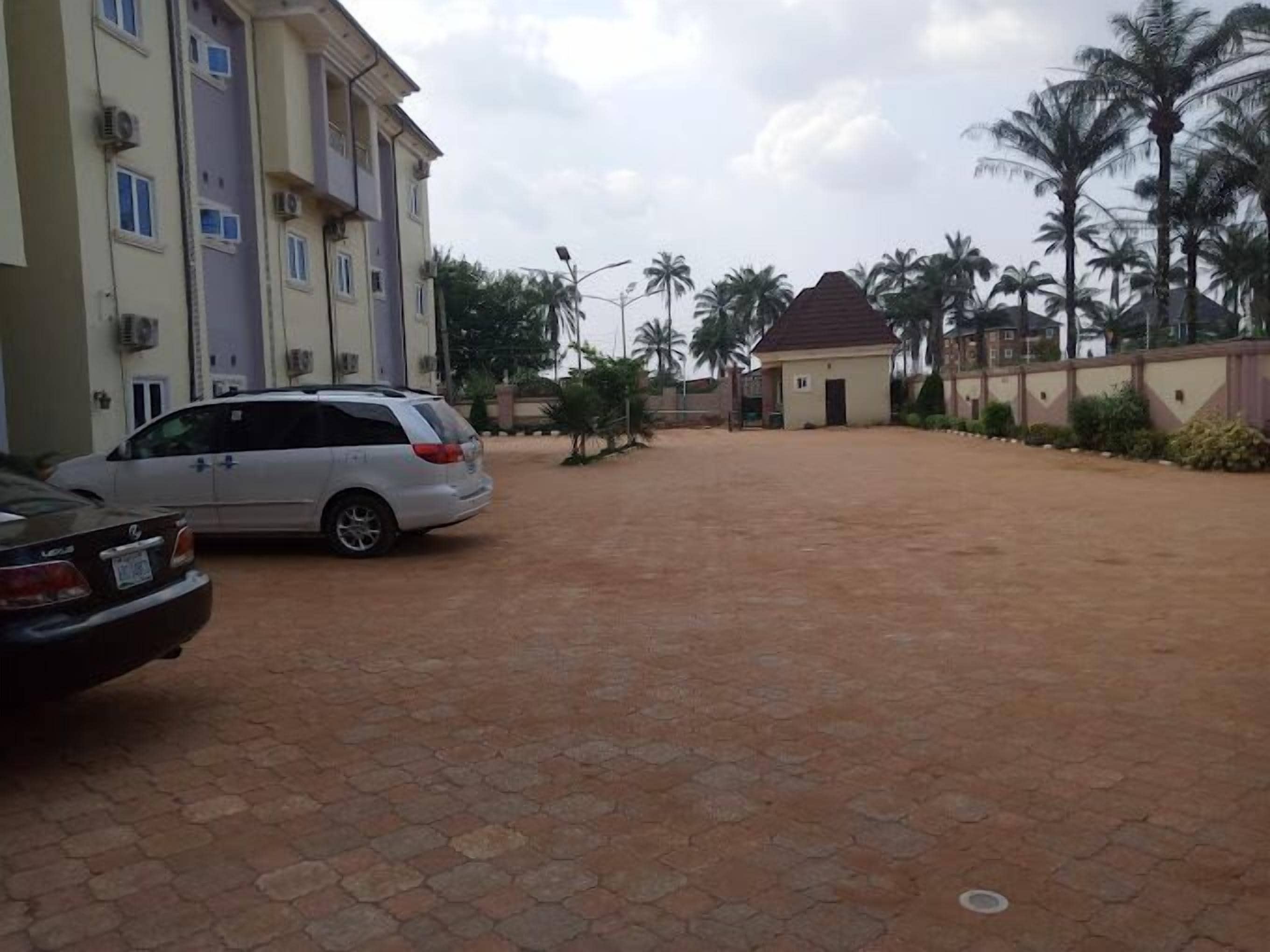 Zona residencial con entrada pavimentada, coches estacionados y un edificio con varias ventanas y unidades de aire acondicionado.