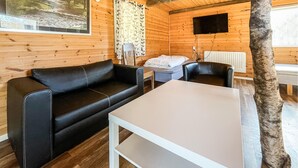 A wooden cabin interior with a black leather sofa, a white table, and a television mounted on the wall. - 1 bedroom cozy home in Huaröd (Huaröd)