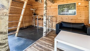 A wooden cabin interior with a black leather sofa, a white table, a ladder, birch trees, and a framed picture on the wall. - 1 bedroom cozy home in Huaröd (Huaröd)