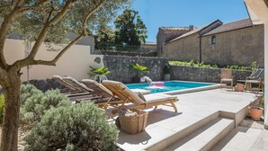 Un espace piscine avec des chaises longues, un mur en pierre et une plante en pot.