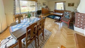 A spacious living room with a fireplace, a dining area with a wooden table and chairs, and a kitchen area with a wooden cabinet and a television.