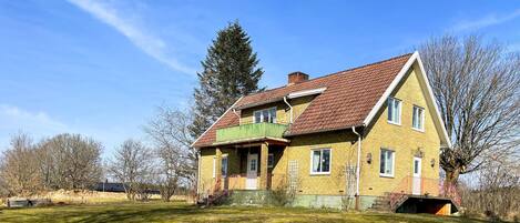 A two-story house with a red-tiled roof, a green porch, and a small front yard.