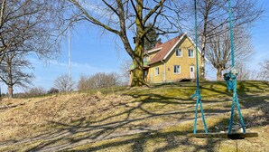 A house with a sloped roof, surrounded by trees and a grassy hill.
