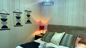 Ein ordentlich bezogenes Bett mit Kissen und Decke, eine Nachttischlampe und Wandbilder.