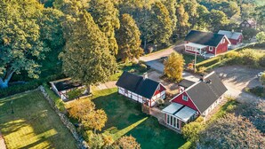 A rural property with multiple red and white buildings, surrounded by dense forest and a well-maintained lawn.