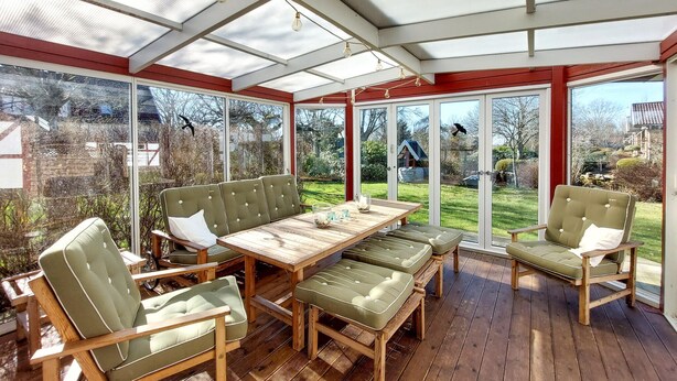 A conservatory with a wooden deck, green cushioned seating, and a glass table.