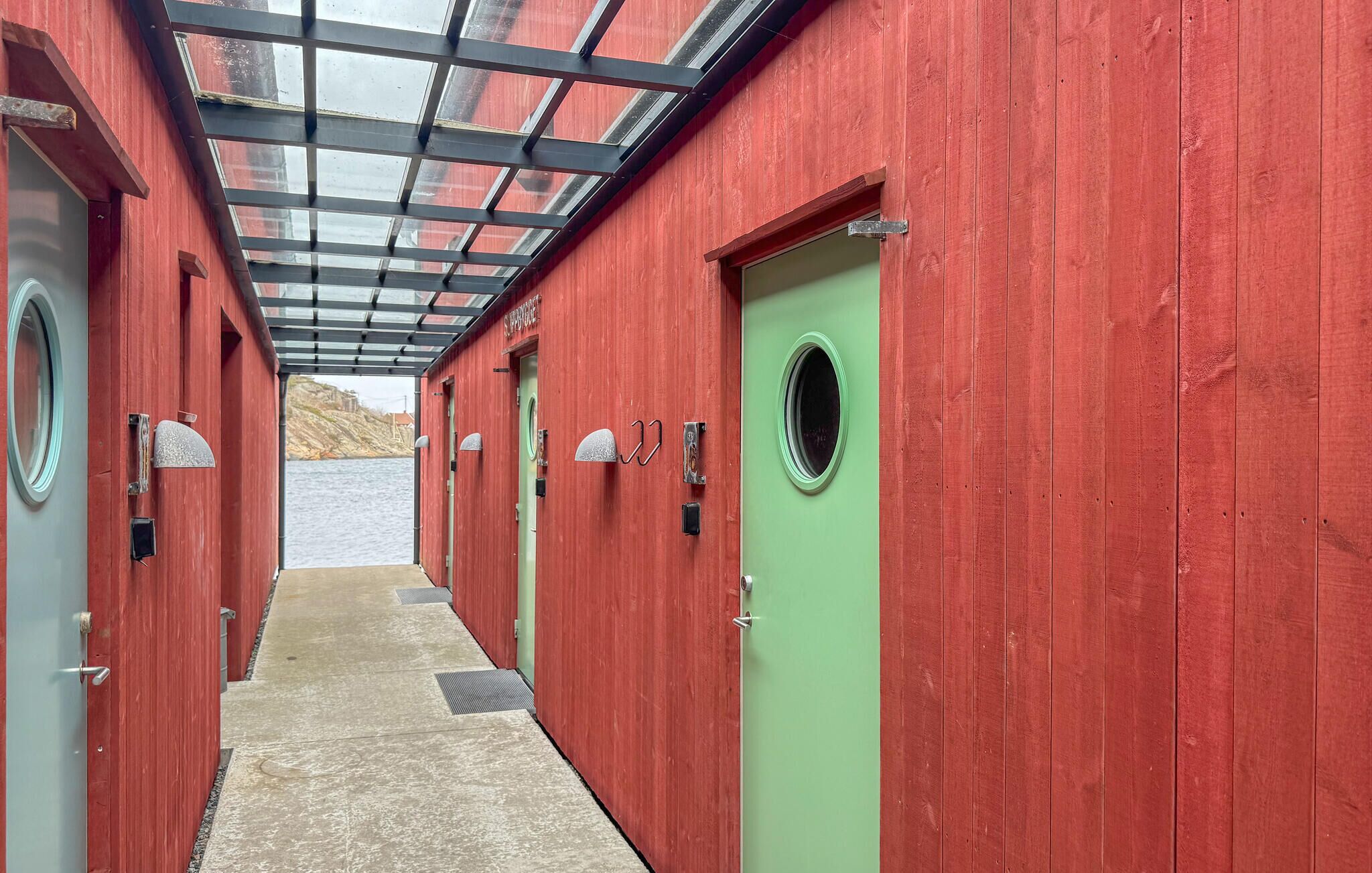 A row of red and green cabins with a glass roof, a concrete floor, and a view of a body of water.