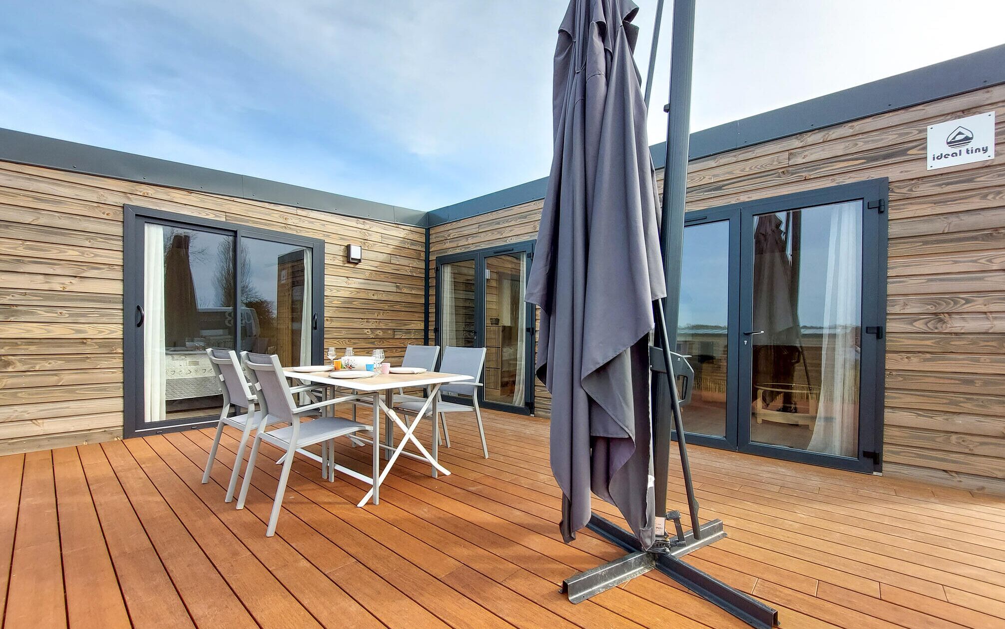 A wooden deck with a table and chairs, a covered umbrella, and a sliding glass door.