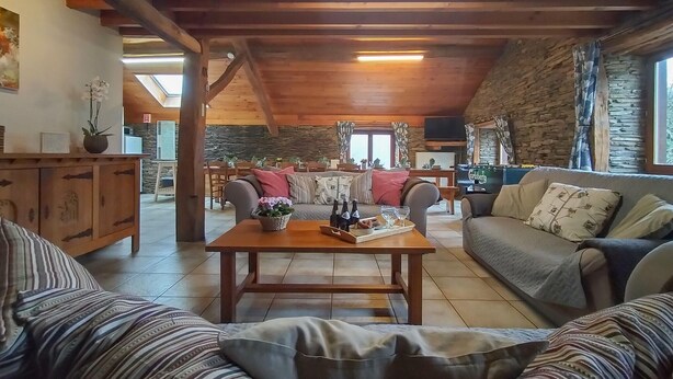 Ein gemütliches Wohnzimmer mit Holzboden, Steinwänden, einer Couch, einem Couchtisch mit Flaschen und Gläsern sowie einem Steinkamin.