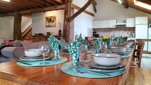 Ein Esszimmer mit Esstisch, Geschirr, Schüsseln und Gläsern, im Hintergrund eine Küche.