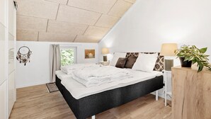 Une chambre moderne avec un grand lit, une table de chevet avec une lampe, une plante en pot et un attrape-rêves accroché au mur.