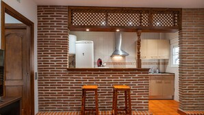 A kitchen with a brick wall, wooden bar stools, a stainless steel range hood, and a tiled backsplash.
