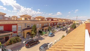 A residential street with terracotta-tiled houses, a clear sky, and parked cars.