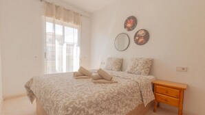 A bedroom with a large bed, two bedside tables, a mirror, and a window with curtains.