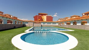 A swimming pool with a white edge, surrounded by a well-maintained lawn, and a building with red-tiled roofs in the background.