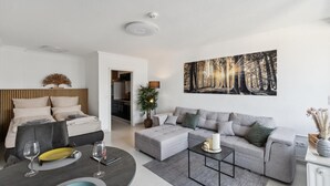 A modern living room with a bed, a grey sofa, a coffee table, and a painting of a forest.