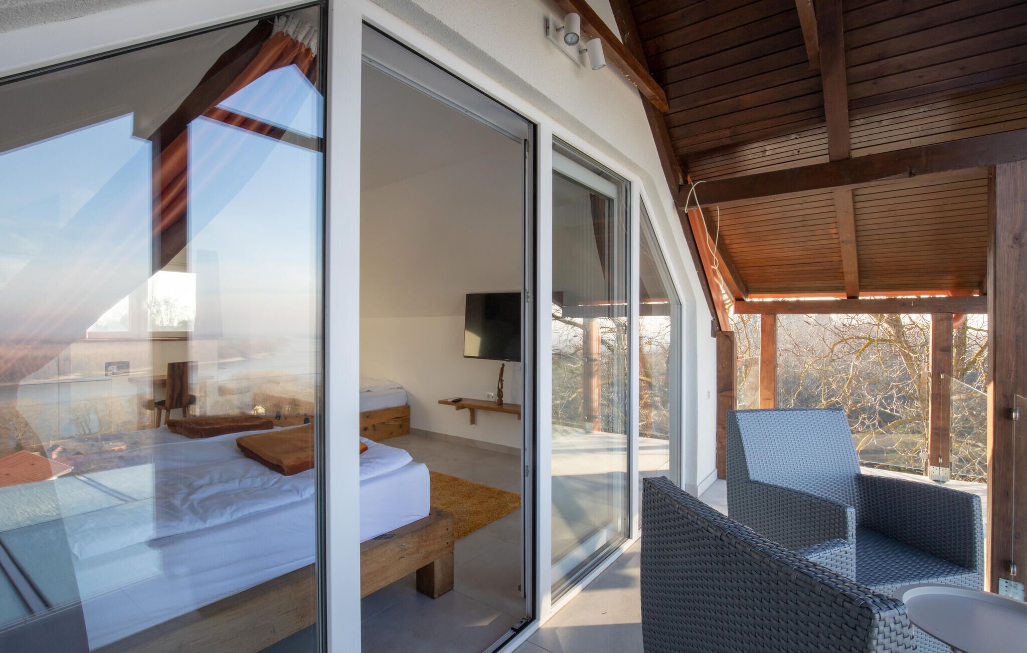 Un dormitorio moderno con puerta de cristal que da a un balcón, una cama, una mesita de noche y un televisor.