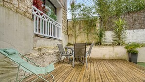 Eine Terrasse mit Tisch, Stühlen und einem Liegestuhl, außerdem Kübelpflanzen.