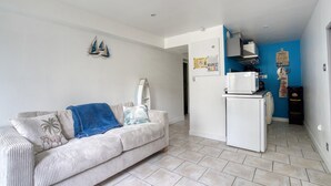 Ein Wohnzimmer mit einer Couch, einem Couchtisch und einer Küchenzeile inklusive Mikrowelle und Kühlschrank.
