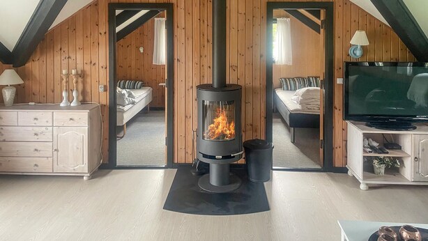 A cozy room with a central wood-burning stove, two beds, a television, and a dresser.