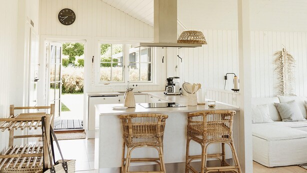 A bright kitchen with white cabinetry, a central island, wicker chairs, and a white sofa in a room with wooden floors and white walls. - Cozy home in Nordborg with WiFi (Nordborg)