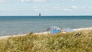 A beach with two striped umbrellas and a sailboat in the distance. - Cozy home in Nordborg with WiFi (Nordborg)