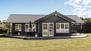 A two-story wooden house with a tiled roof, a covered patio with outdoor furniture, and a well-maintained lawn. - Cozy home in Nordborg with WiFi (Nordborg)