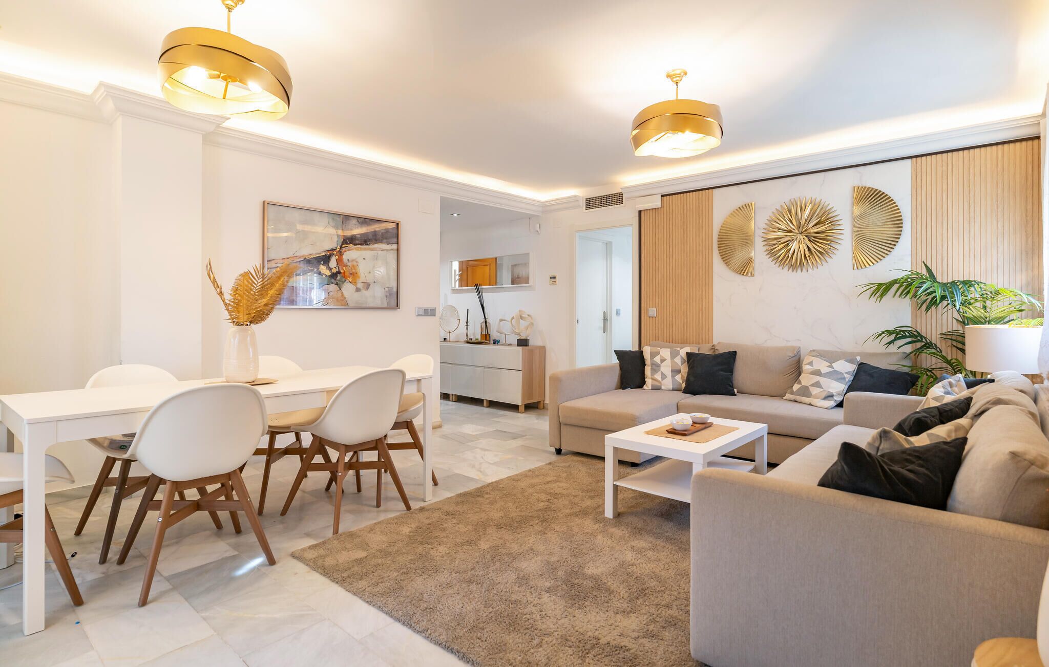 Un salon moderne avec un coin repas, comprenant un ensemble de canapés, une table basse et une table à manger avec des chaises. On y trouve également des panneaux décoratifs et un grand tableau au mur.