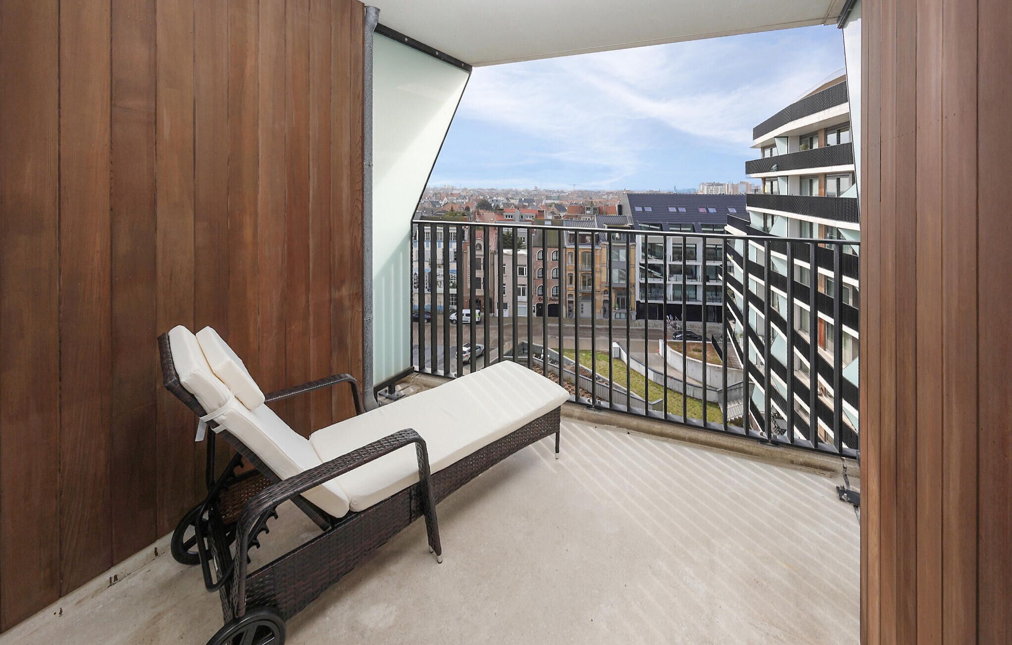 Uma varanda com uma única poltrona de descanso, vista para a cidade e uma parede de madeira.