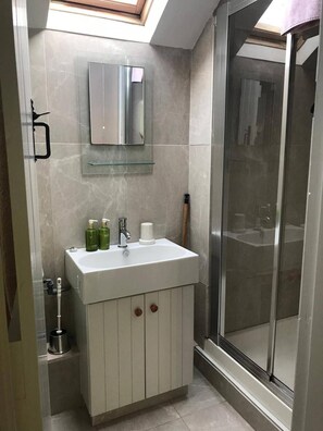 Un baño con tragaluz, lavabo con artículos de aseo y zona de ducha.