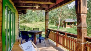 A wooden deck with a table and chairs, overlooking a grassy area with trees and a small cabin. - Cozy home in Czaplinek with lake view (Czaplinek)